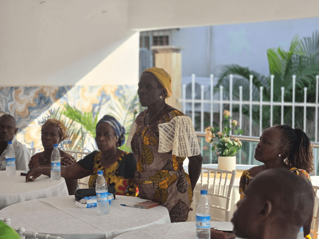 Une participante debout s'exprime lors d'une réunion d'échanges autour d'une table avec d'autres femmes assises.
