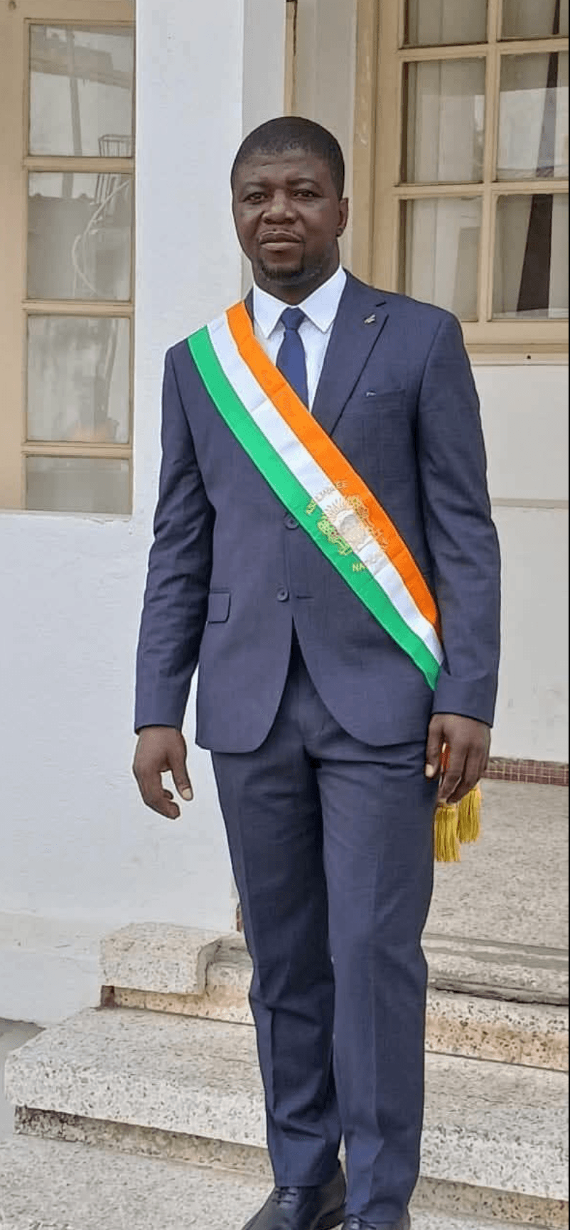 Portrait en pied de l'Honorable Innocent Yao portant l'écharpe tricolore de député.
