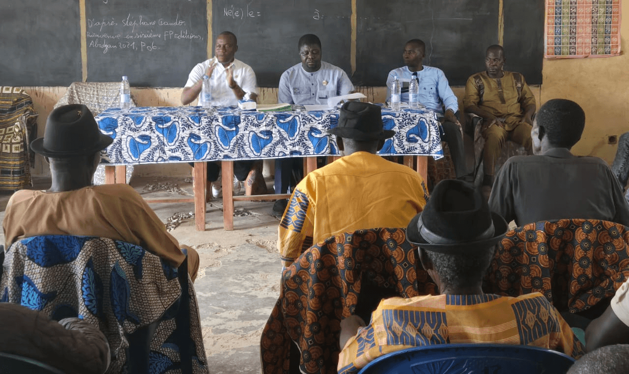 Vue d'ensemble de la salle de classe avec la délégation officielle à la table et les notables de dos au premier plan.