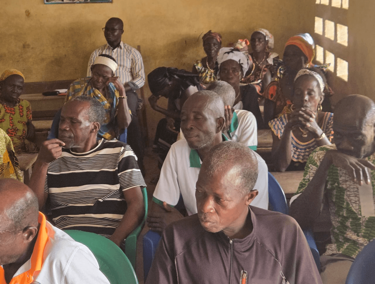 Groupe d'habitants et de femmes attentifs assis lors de la rencontre de restitution.