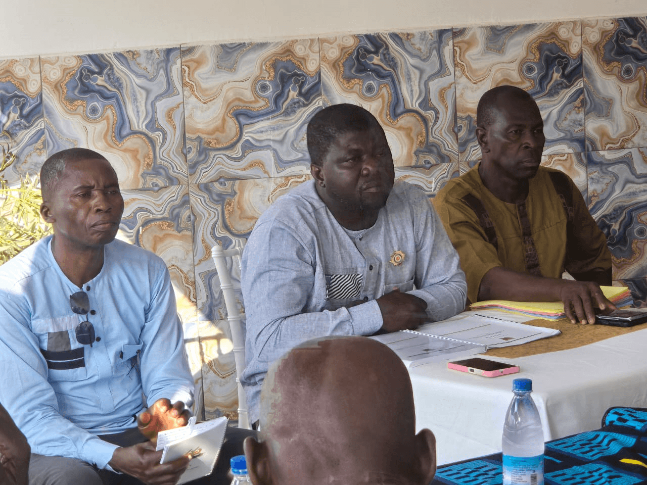 L'Honorable Innocent Yao assis à une table de réunion avec deux collaborateurs.