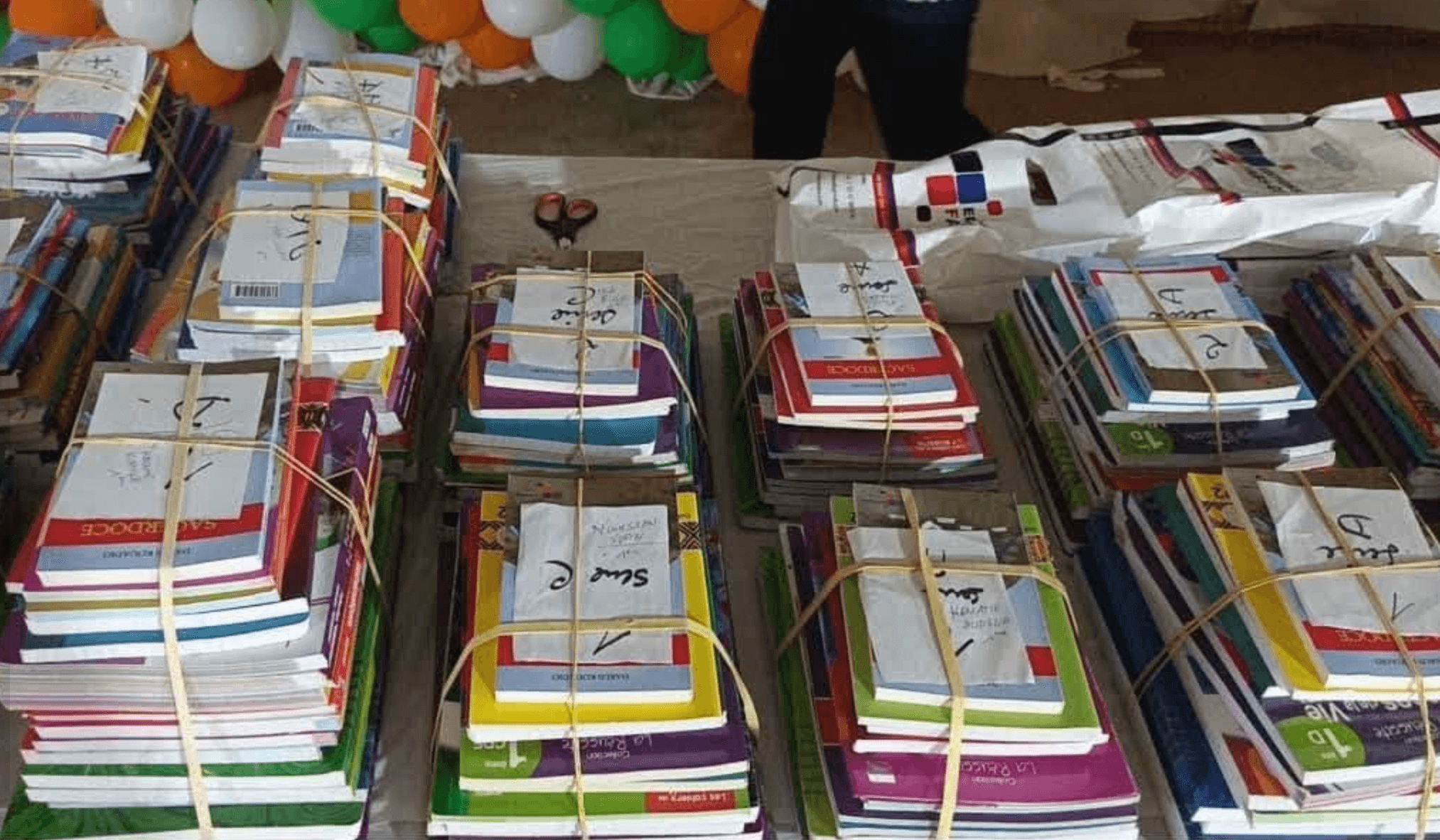 Kits scolaires — cahiers, livres et fournitures — empilés sur une table avant distribution.