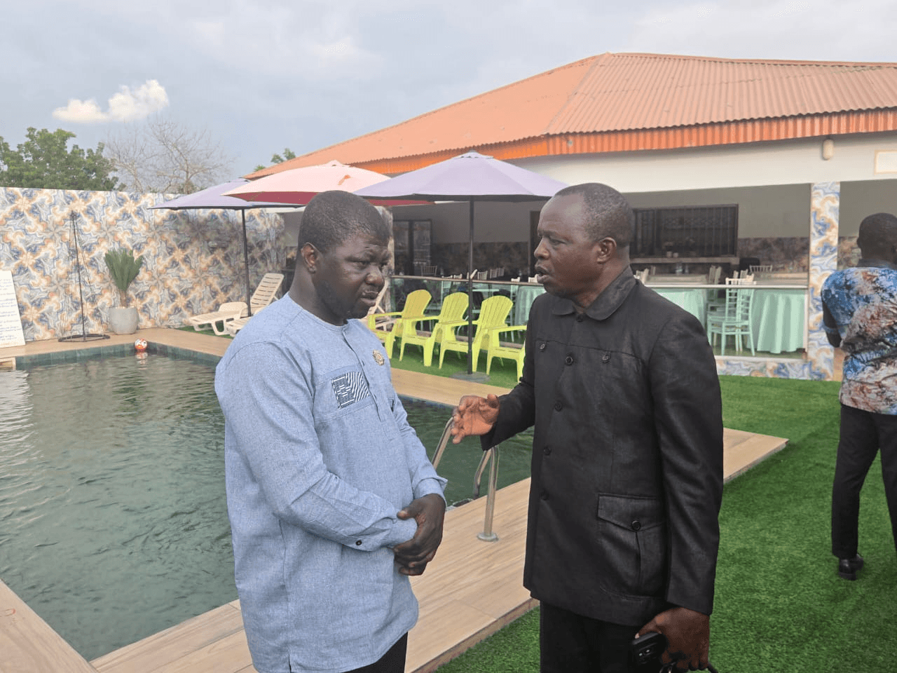 L'Honorable Innocent Yao en discussion avec un homme en costume noir au bord d'une piscine.