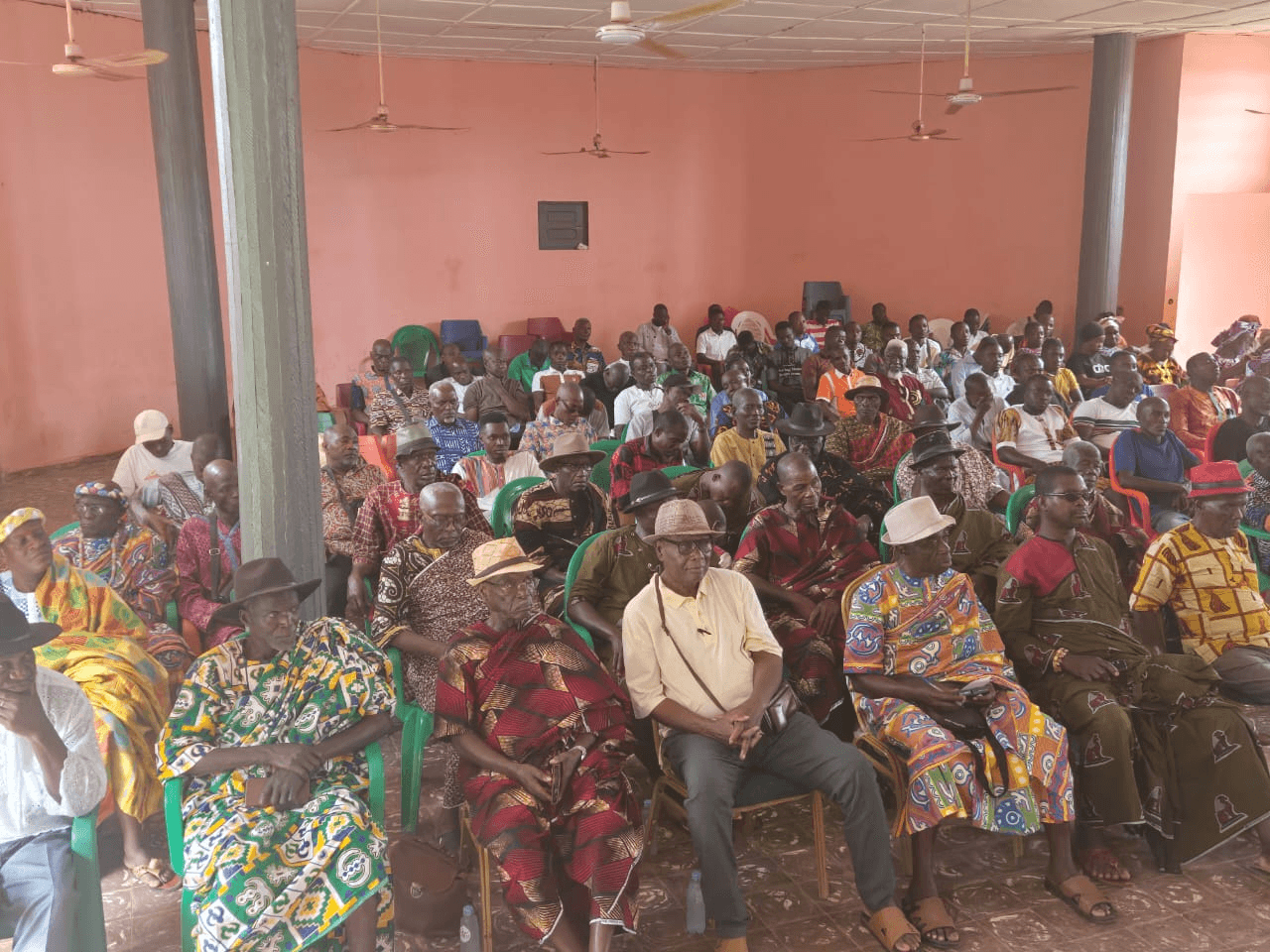 Assemblée de chefs traditionnels ivoiriens en pagnes d'apparat et chapeaux assis dans une grande salle.