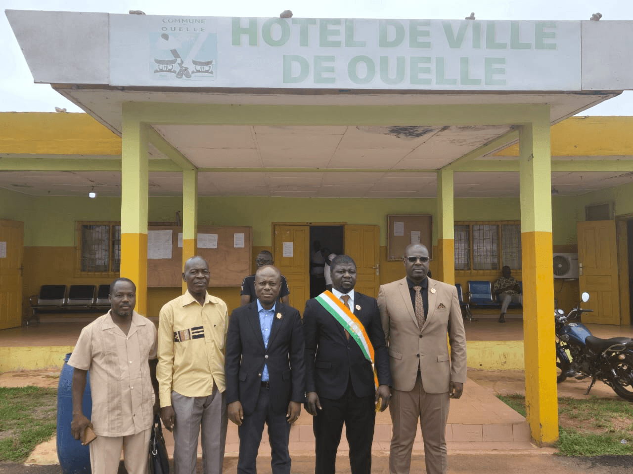L'Honorable Innocent Yao portant son écharpe tricolore entouré de quatre collaborateurs devant l'Hôtel de Ville de Ouellé.