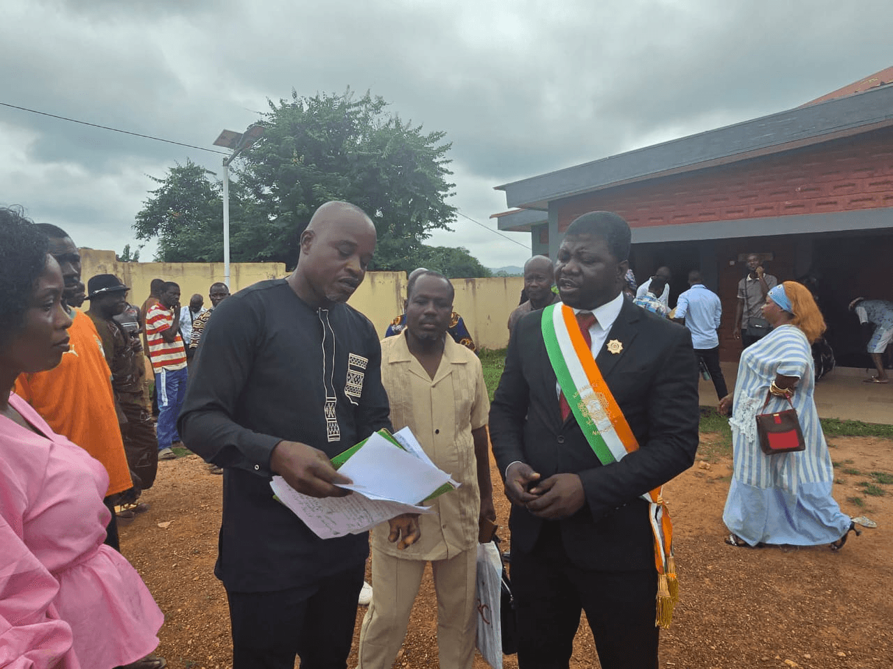 L'Honorable Innocent Yao et son collaborateur examinant des documents écrits en extérieur.