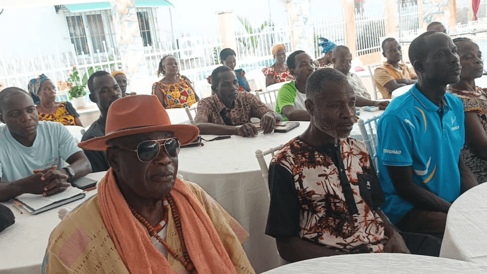 Chef traditionnel avec chapeau orange et collier de perles assis à une table de réunion.