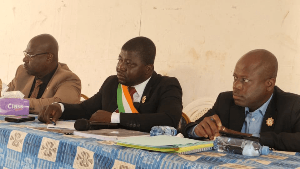 L'Honorable Innocent Yao assis à la tribune officielle entre deux collègues.