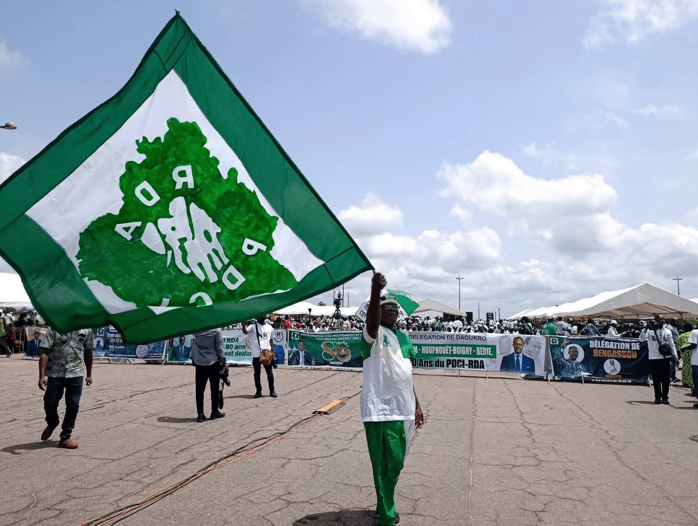 Militant portant le drapeau du PDCI-RDA lors d'un rassemblement de plein air.