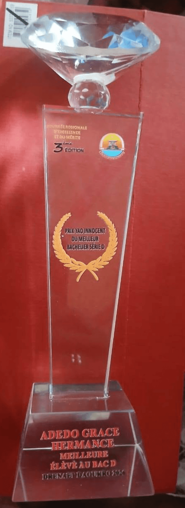Trophée « Prix Yao Innocent du meilleur bachelier série D » décerné à une lauréate, présenté sur fond rouge.
